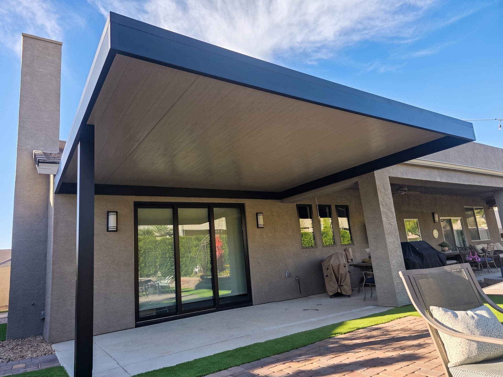 Attached 4K Aluminum patio cover with a solid roof, light wood-look ceiling and dark frame over a sliding door