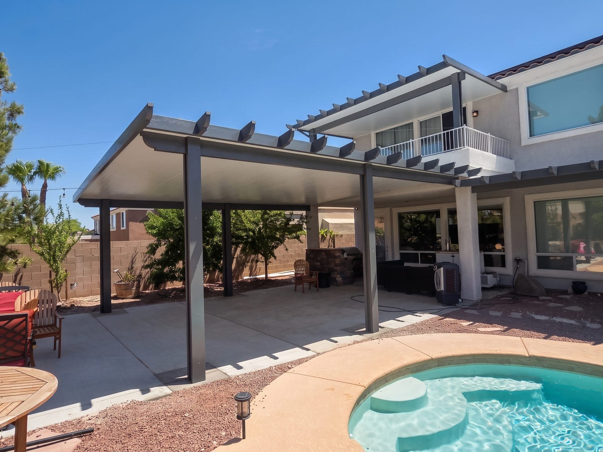 Gray Alumawood solid-roof patio cover with scalloped rafter tails over a backyard patio by a pool, with a second cover over the upstairs balcony
