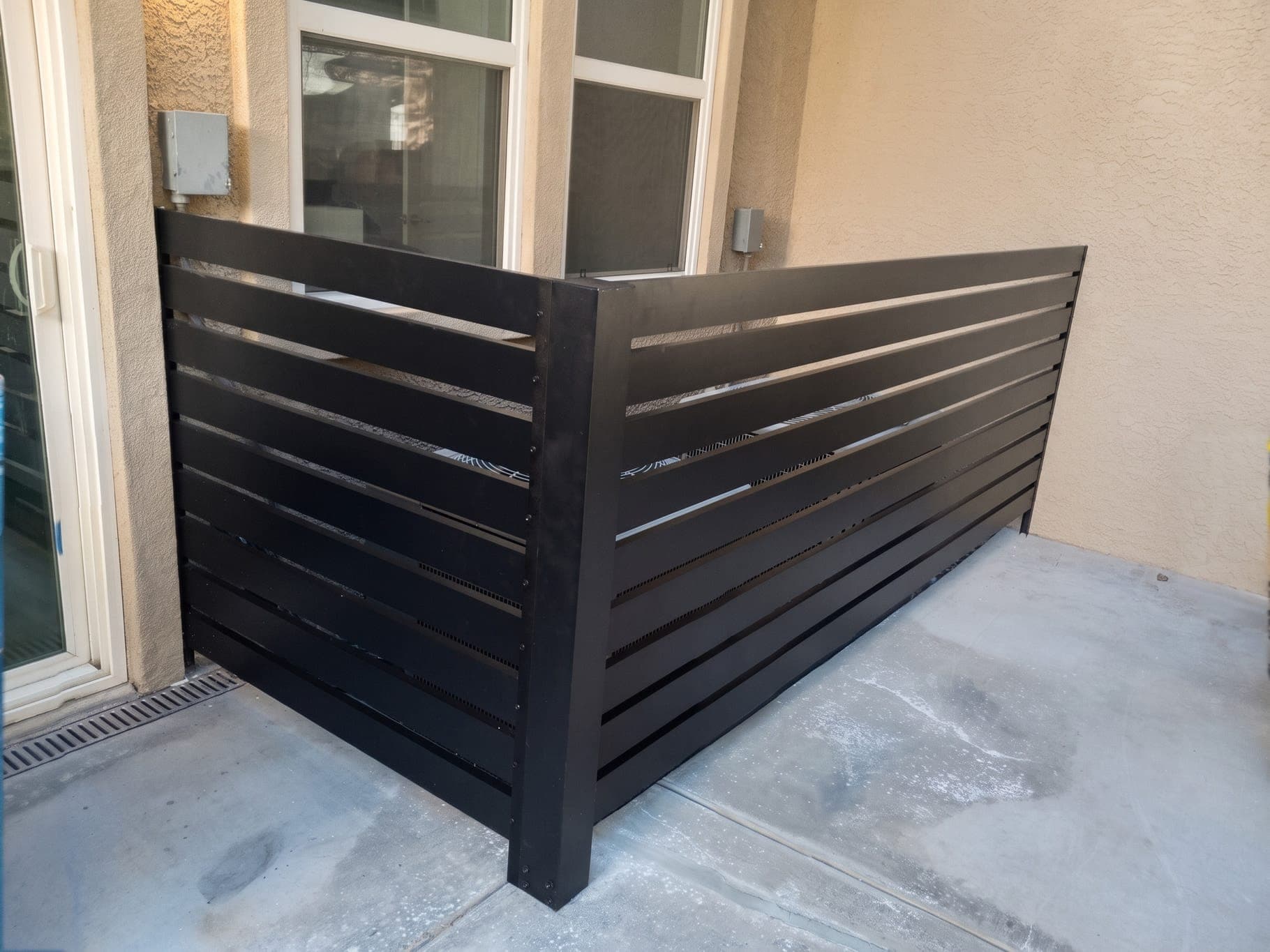 Corner of a black horizontal slat 4K Aluminum equipment screen on a concrete patio
